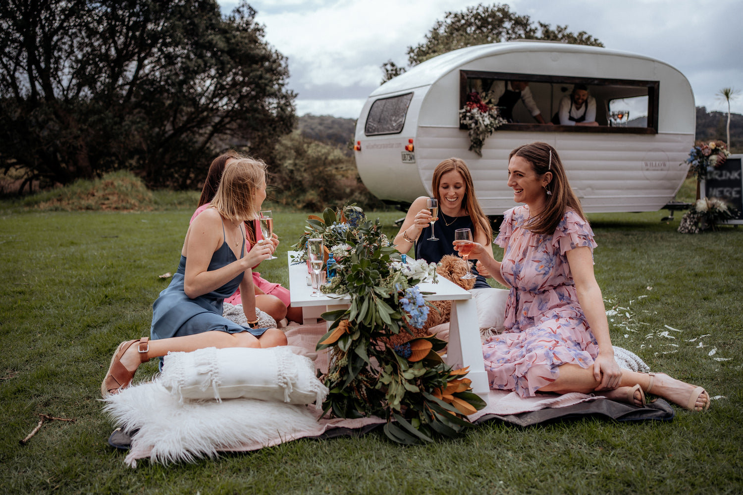Group of ladies drinking champagne around a beautiful low picnic table with rugs and cushions