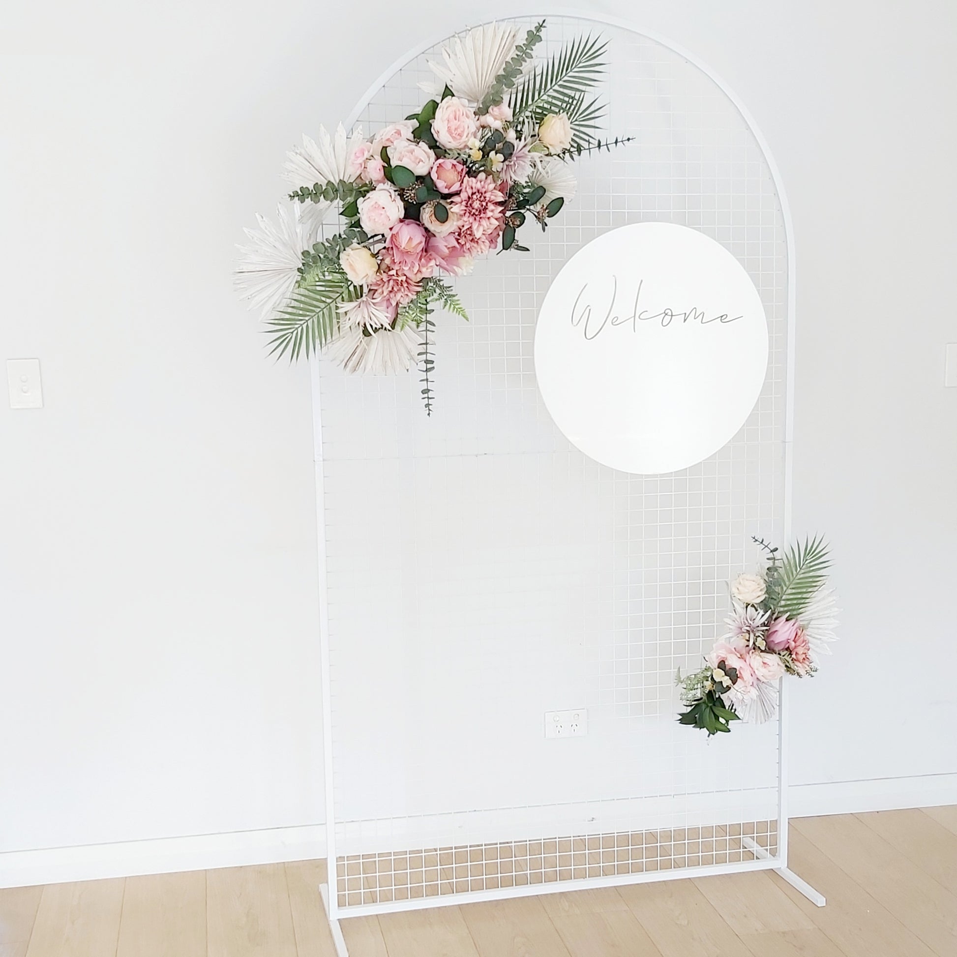 white mesah backdrop with welcome sign and florals 